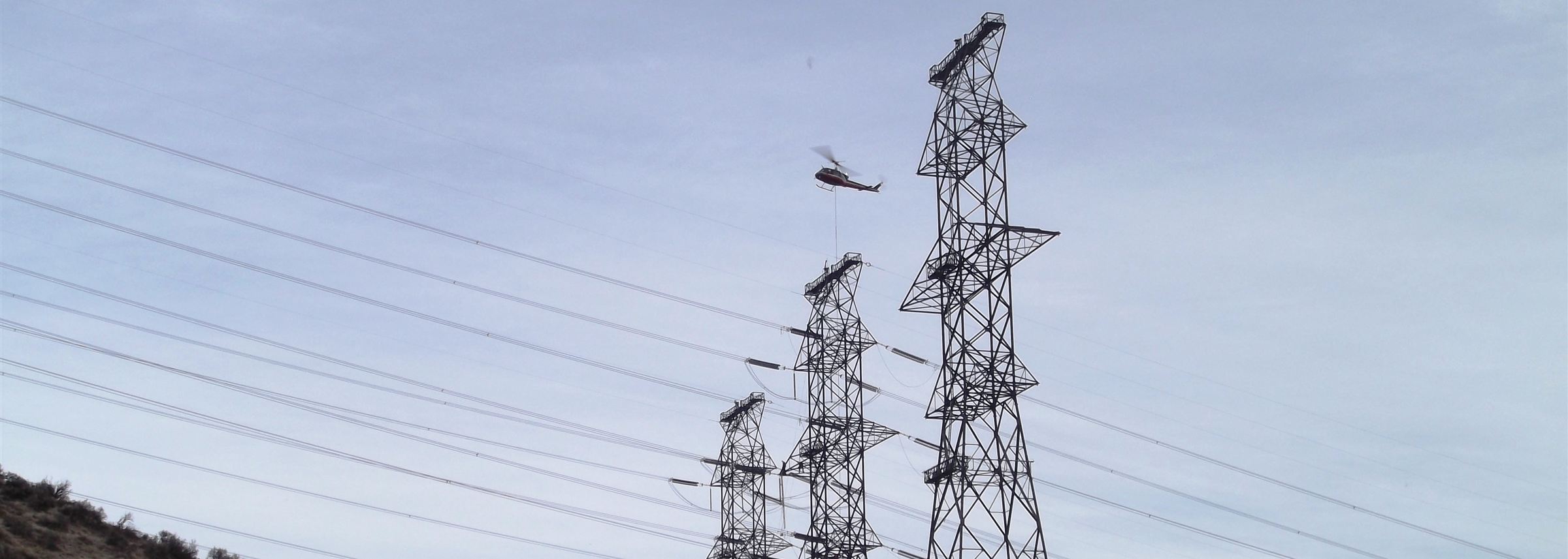 Helicopter working at the tops of new lattice transmission towers during line construction