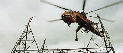 Sky-crane helicopter lowering steel onto a lattice tower under construction