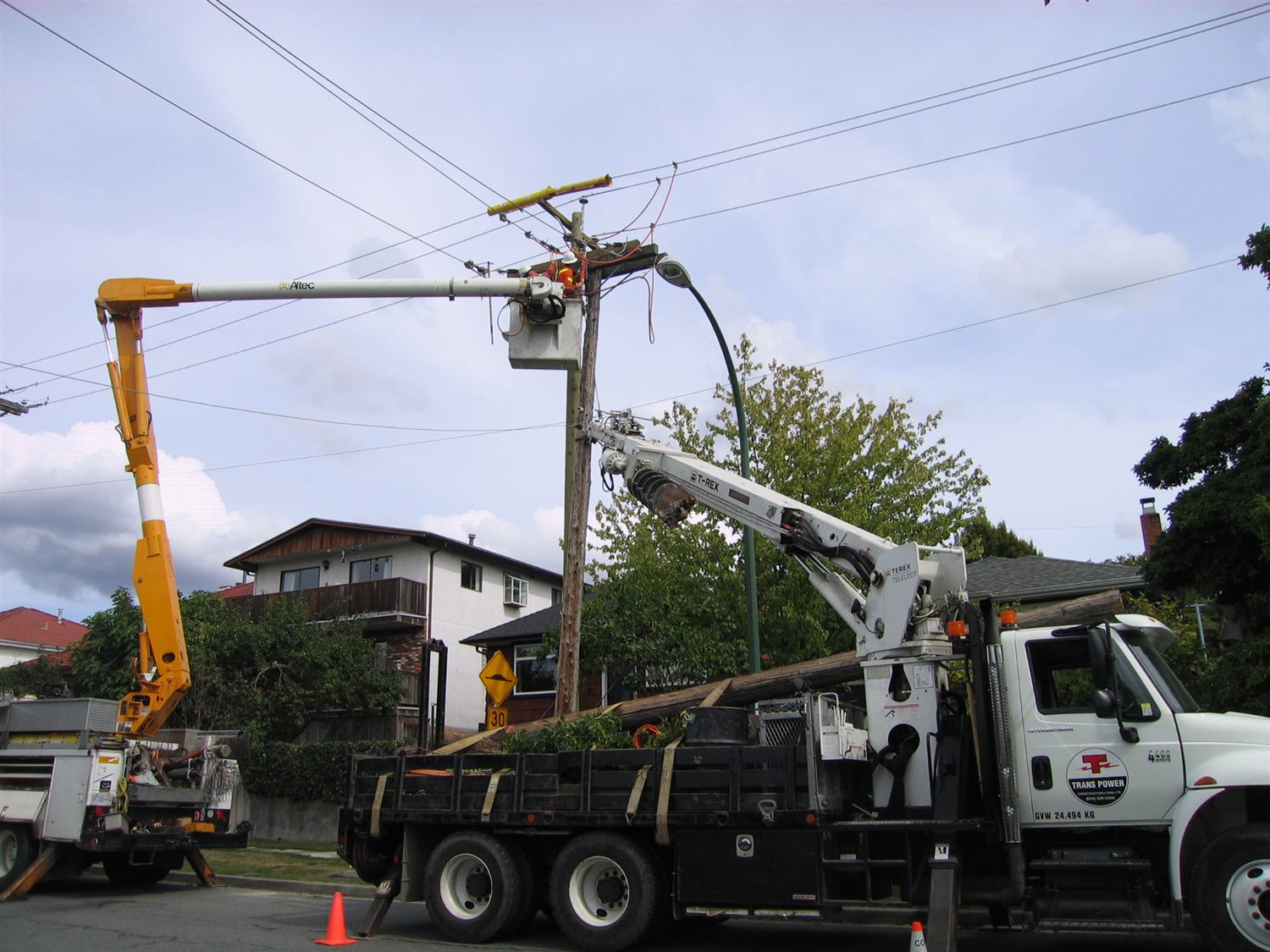 Trans Power boom trucks and a bucket crew replacing a distribution pole on a residential street